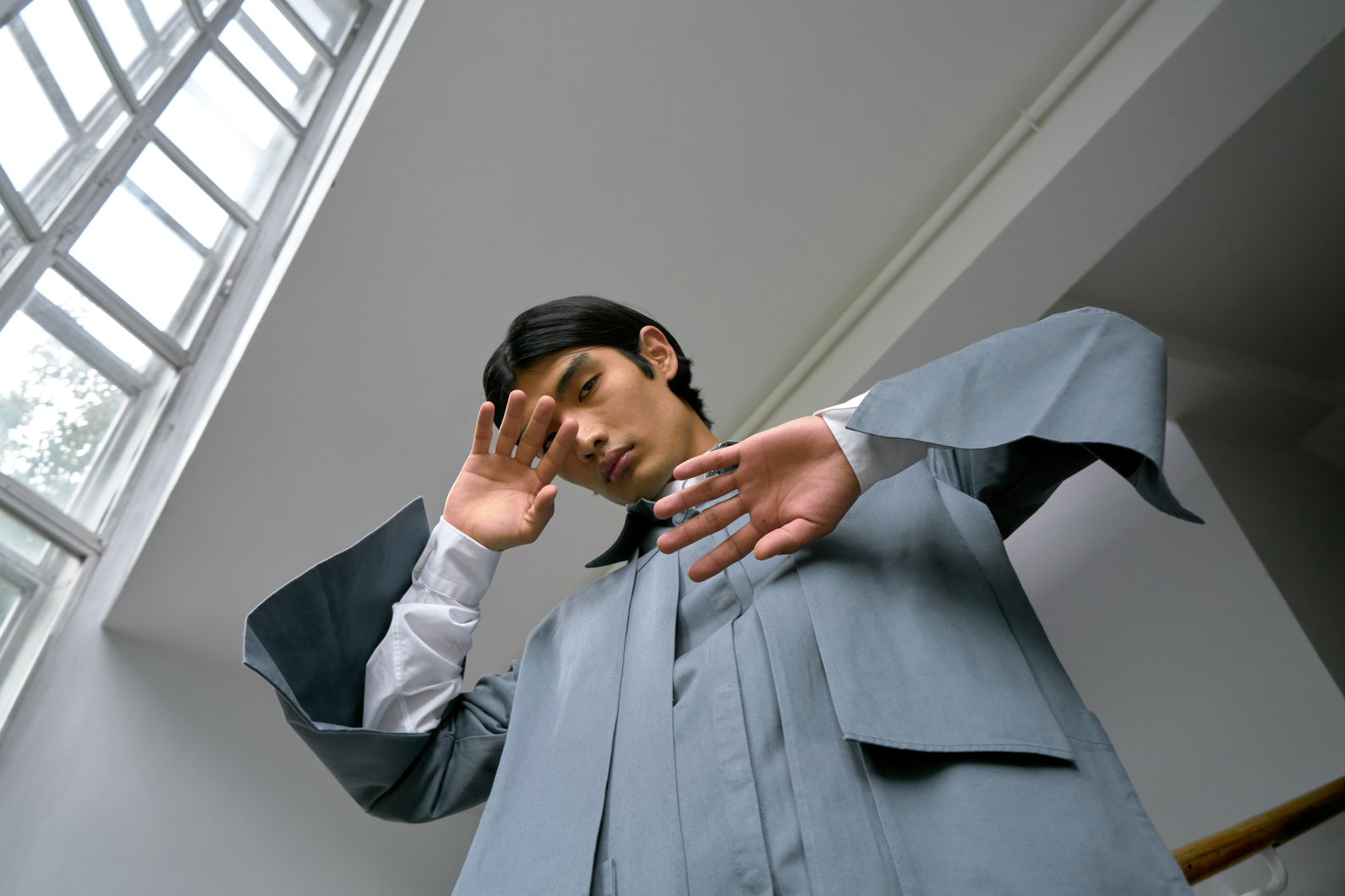 A Fashionable Man Seriously Projecting at the Camera while Standing Near the Glass Window